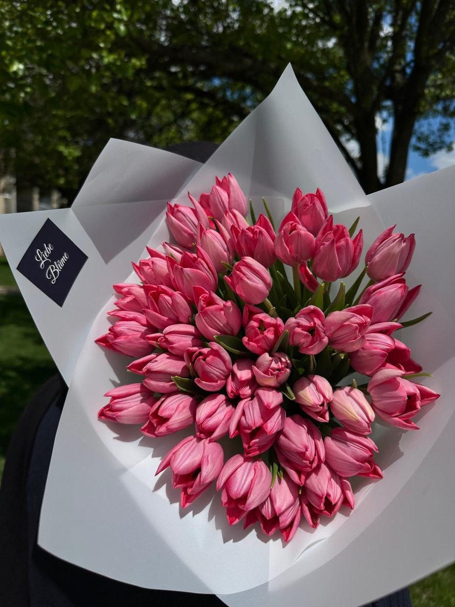 Large bouquet of pink tulips in white wrap with the black Liebe Blüme label, held outdoors