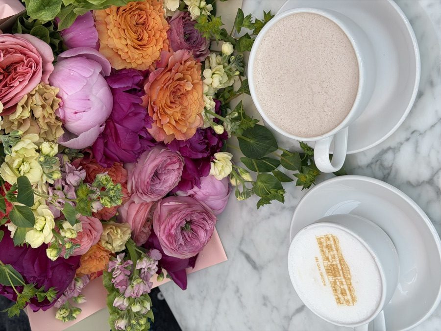 Colorful peony and garden rose bouquet on a marble cafe table beside two lattes