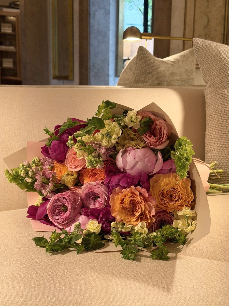 Peony and garden rose bouquet in blush wrap resting on a cream boucle sofa