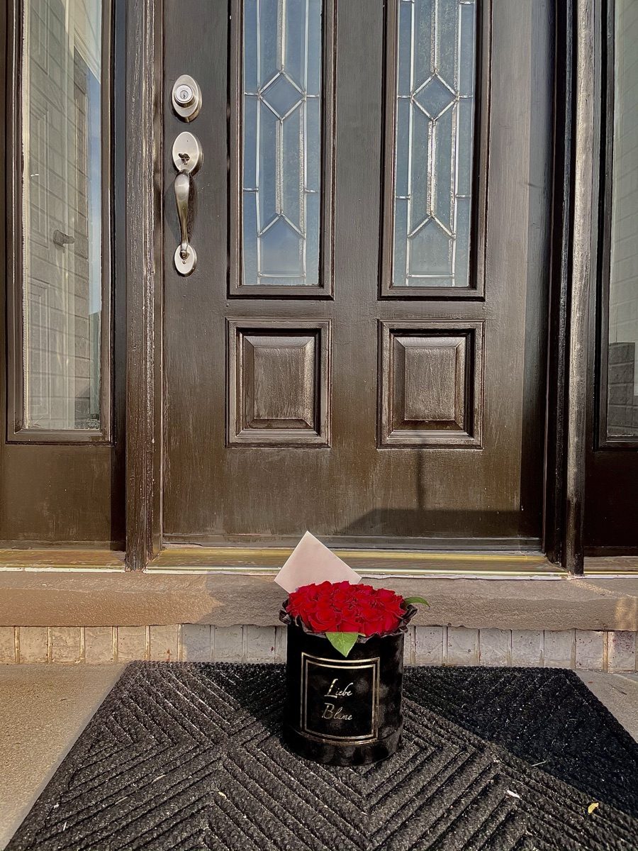Black Liebe Blüme box of red roses with a blush envelope waiting on a doorstep