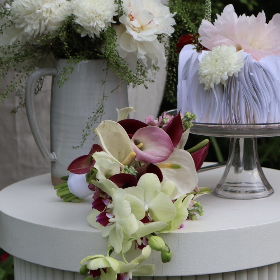Cascading calla lily and orchid bridal bouquet on a white pedestal table with a peony-topped pleated wedding cake