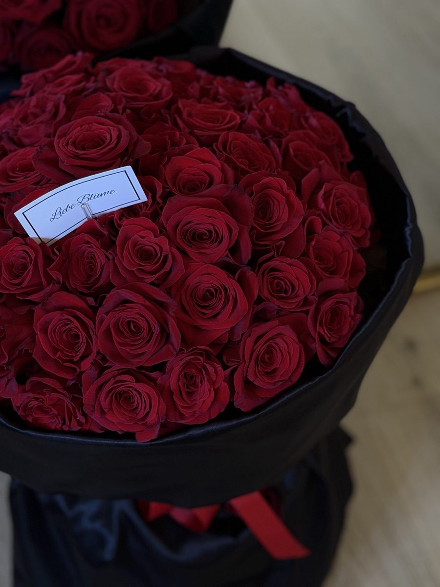 Grand hand-tied dome of deep red roses wrapped in black satin with a Liebe Blüme card