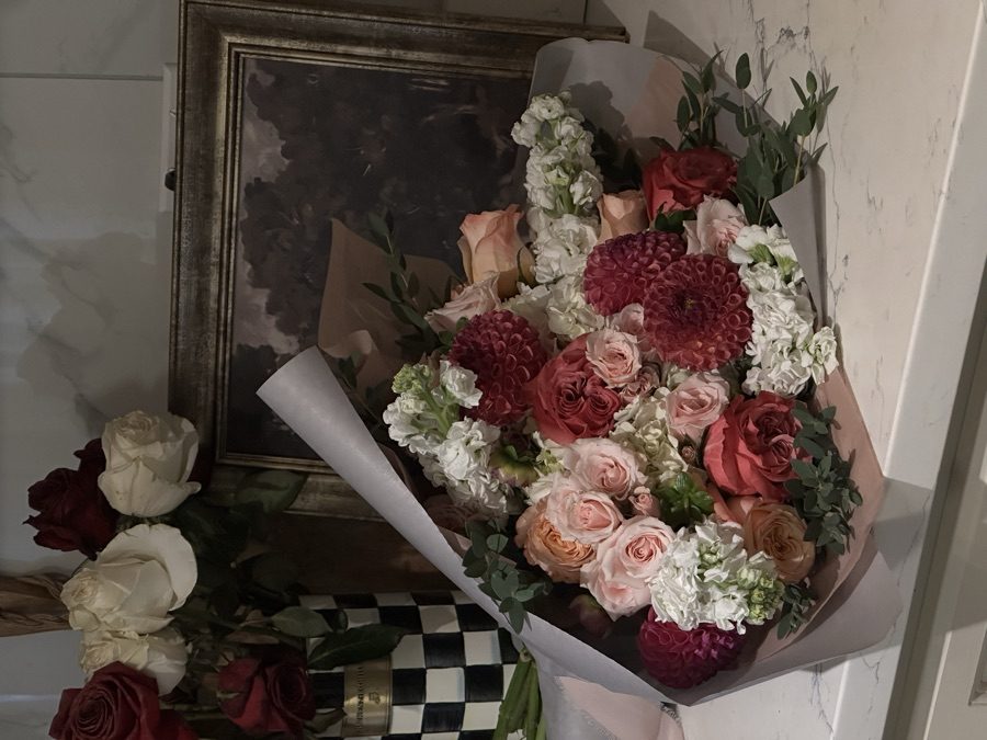 Dahlia and garden rose bouquet in taupe wrap on marble beside a vintage framed painting