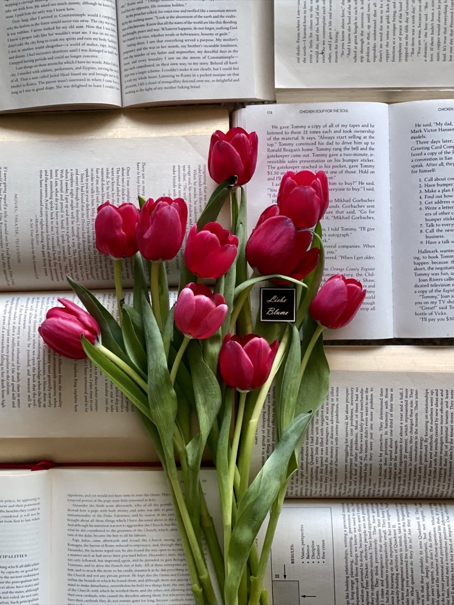Magenta tulips with a black Liebe Blüme tag laid across open book pages