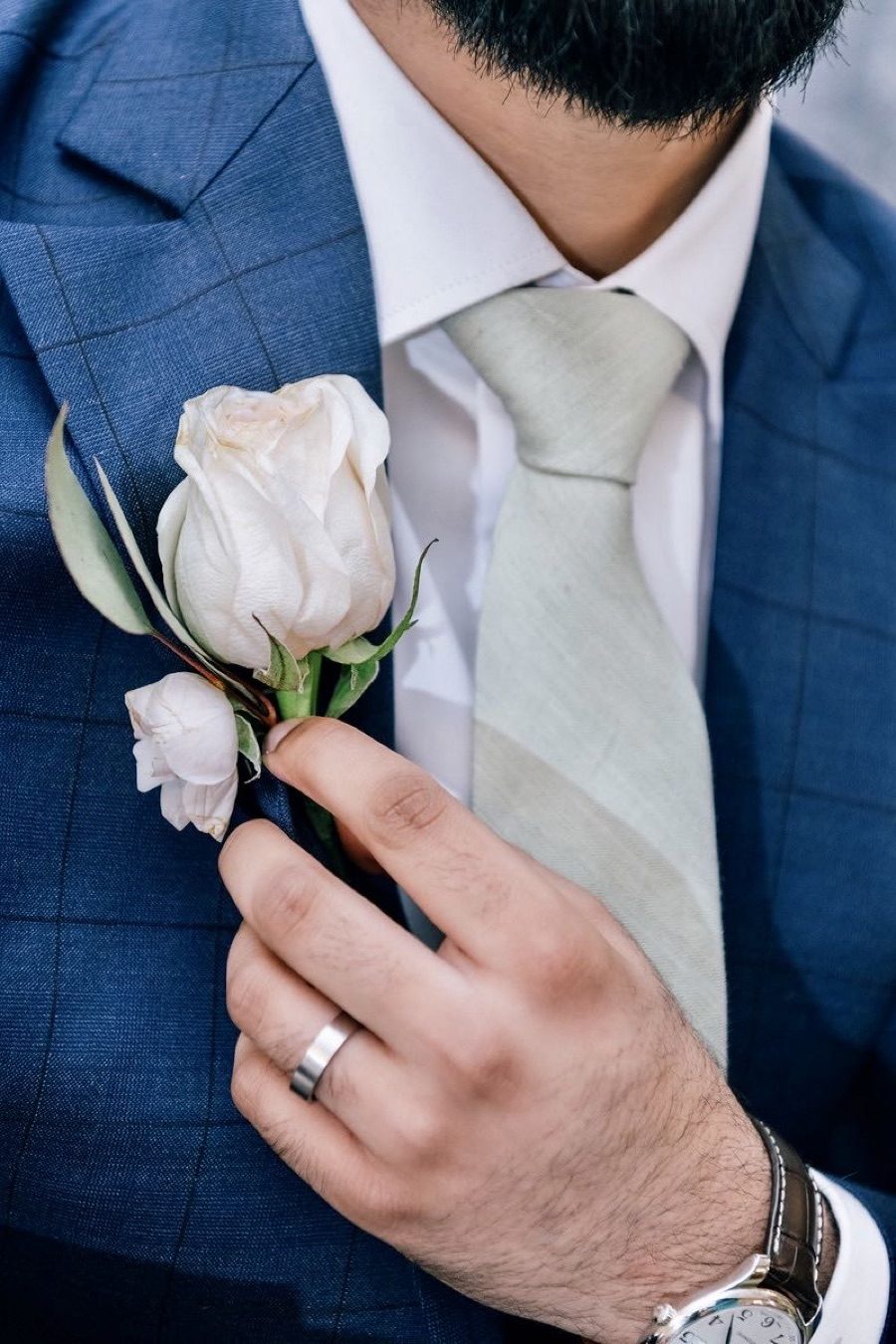Groom in a blue checked suit adjusting a cream spray rose boutonniere