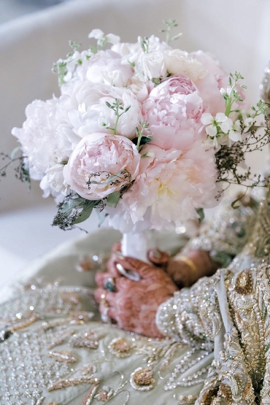 Bride with henna holding a blush and white peony bouquet over a beaded bridal gown