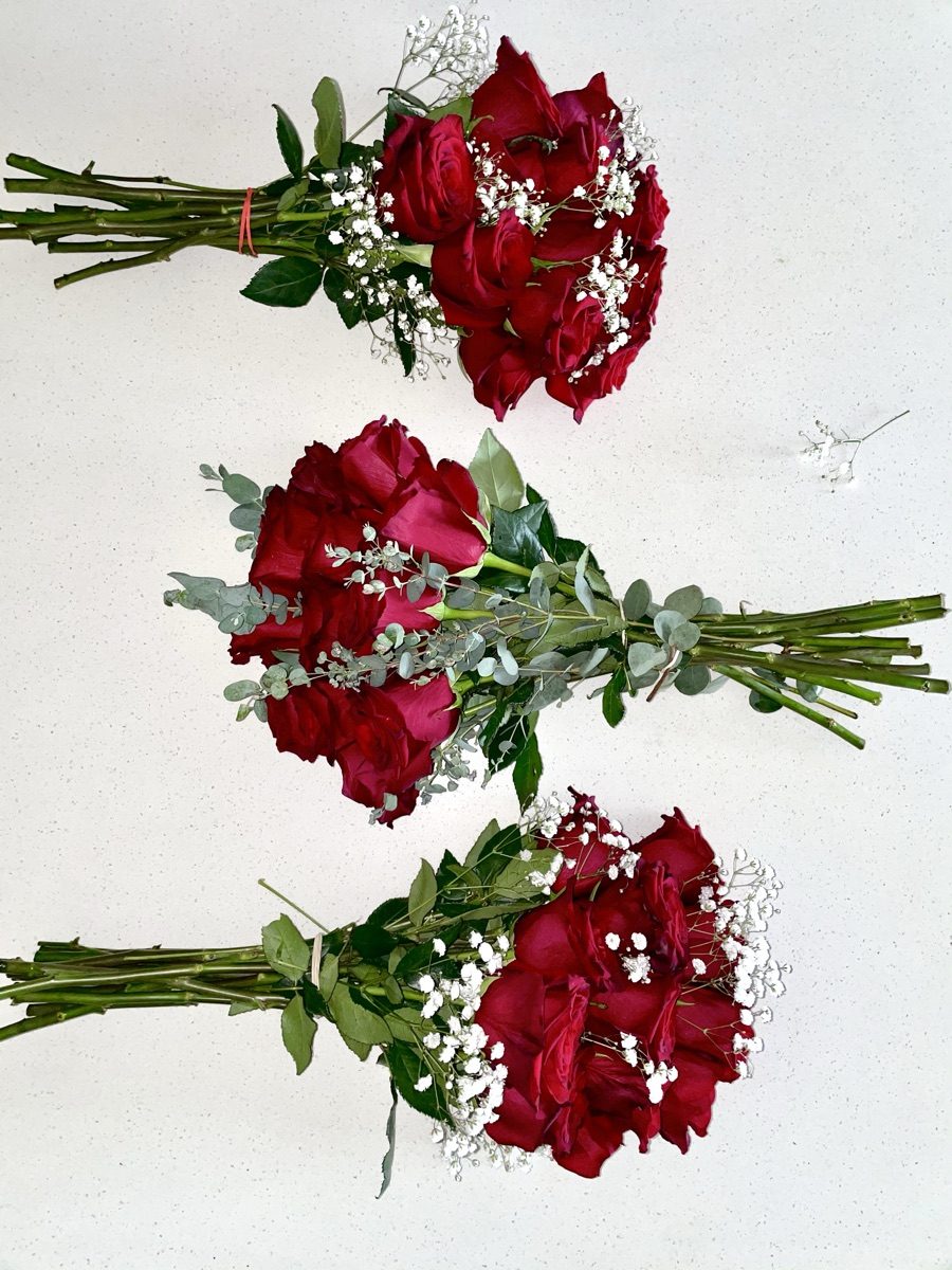 Three hand-tied red rose bouquets with baby's breath laid on a white counter