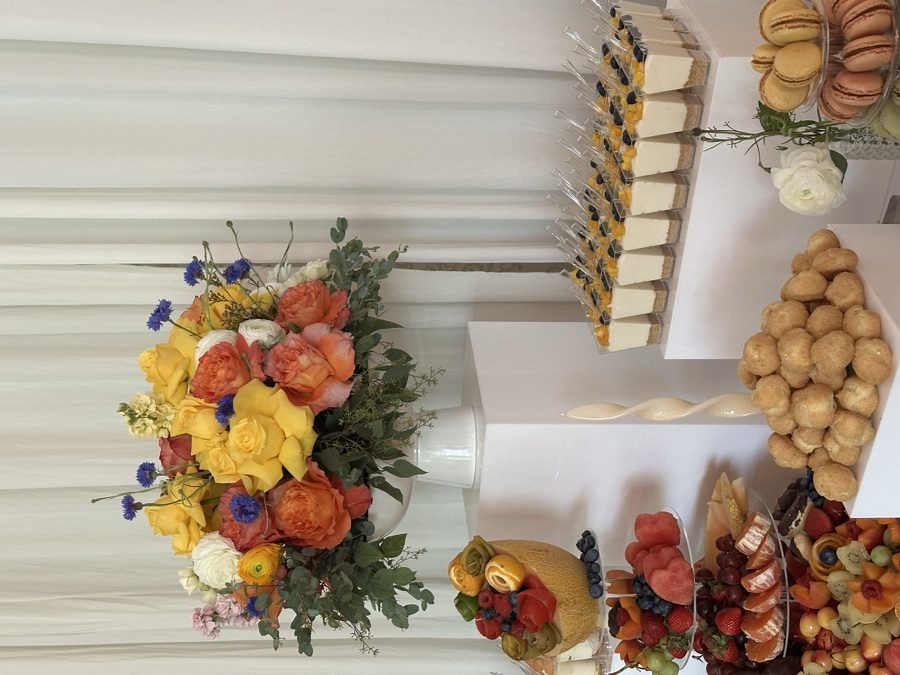 Yellow and coral garden rose arrangement in a white vase on a pedestal at a styled dessert display
