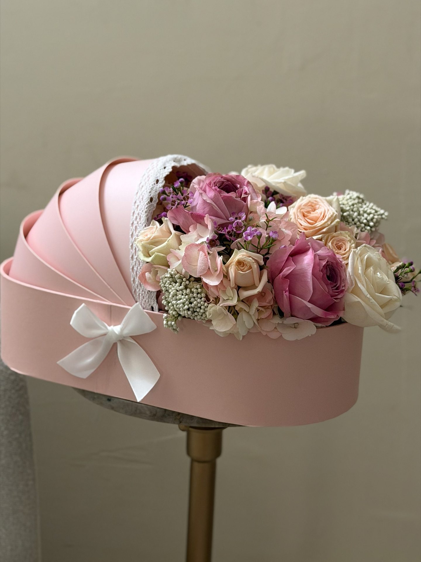 Pink pram-shaped floral arrangement with mauve and cream roses on a gold pedestal stand