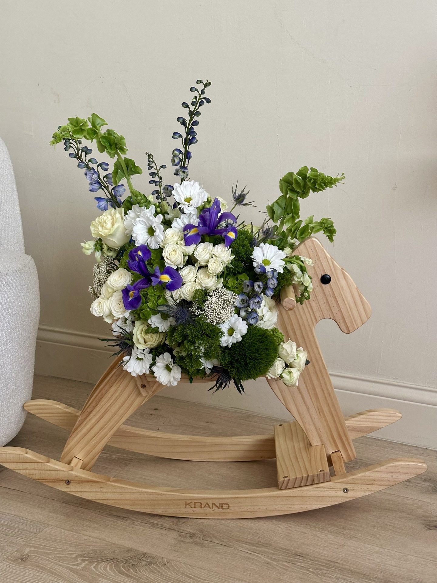Iris, delphinium and white rose arrangement styled on a wooden rocking horse for a new baby