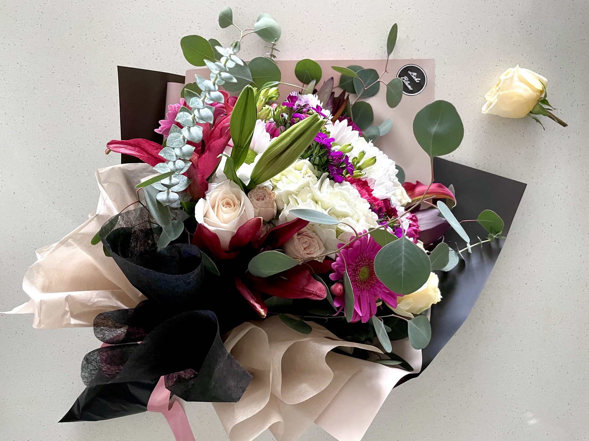 Lily, rose and gerbera bouquet with eucalyptus in black and cream Liebe Blüme wrap, flat lay
